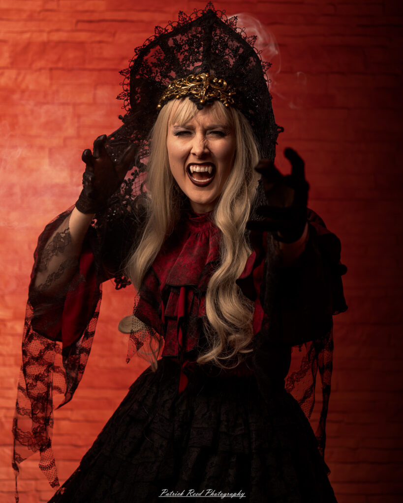 Portrait of a woman in vampire cosplay named Lady Thorn, photographed on June 28, 2025. She is posed against a vivid red background, styled with gothic elements and dramatic expression.