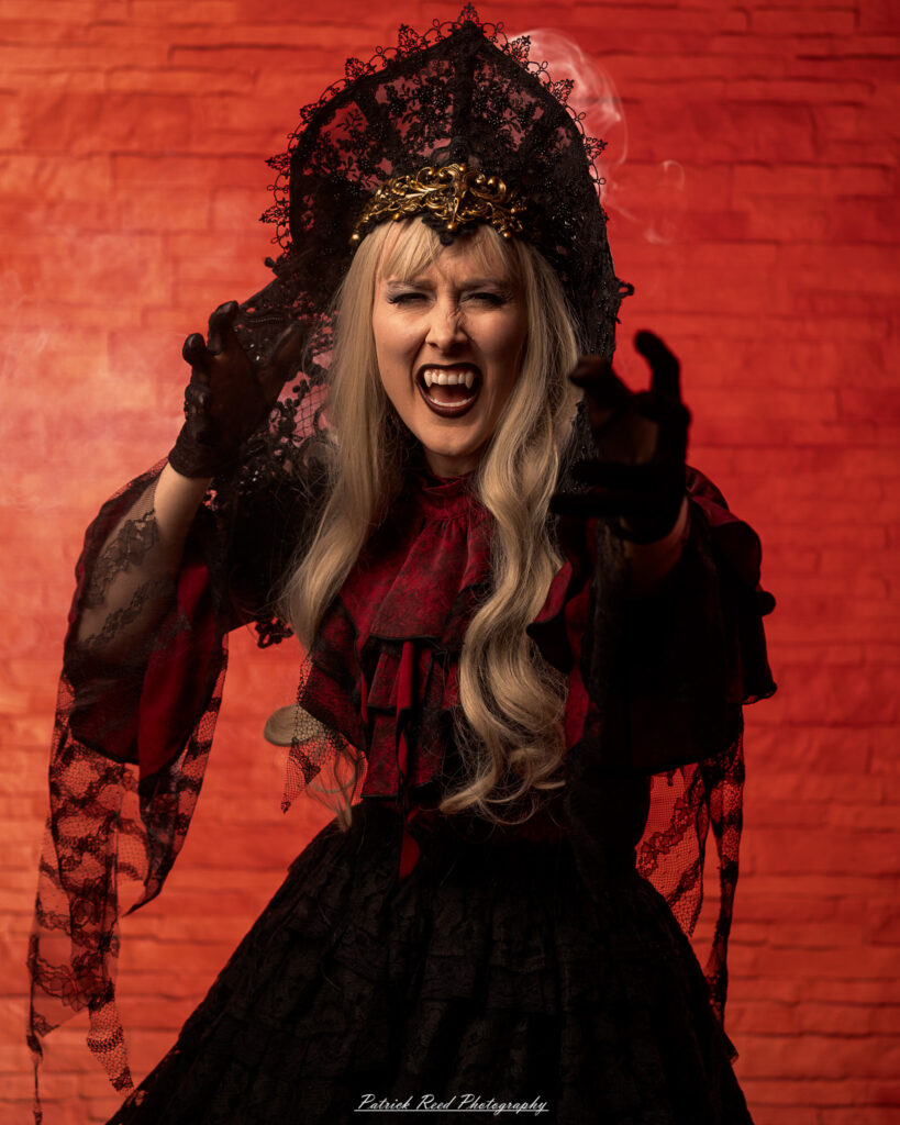 Alt text: Portrait of a woman in vampire cosplay named Lady Thorn, photographed on June 28, 2025. She is posed against a vivid red background, styled with gothic elements and dramatic expression.