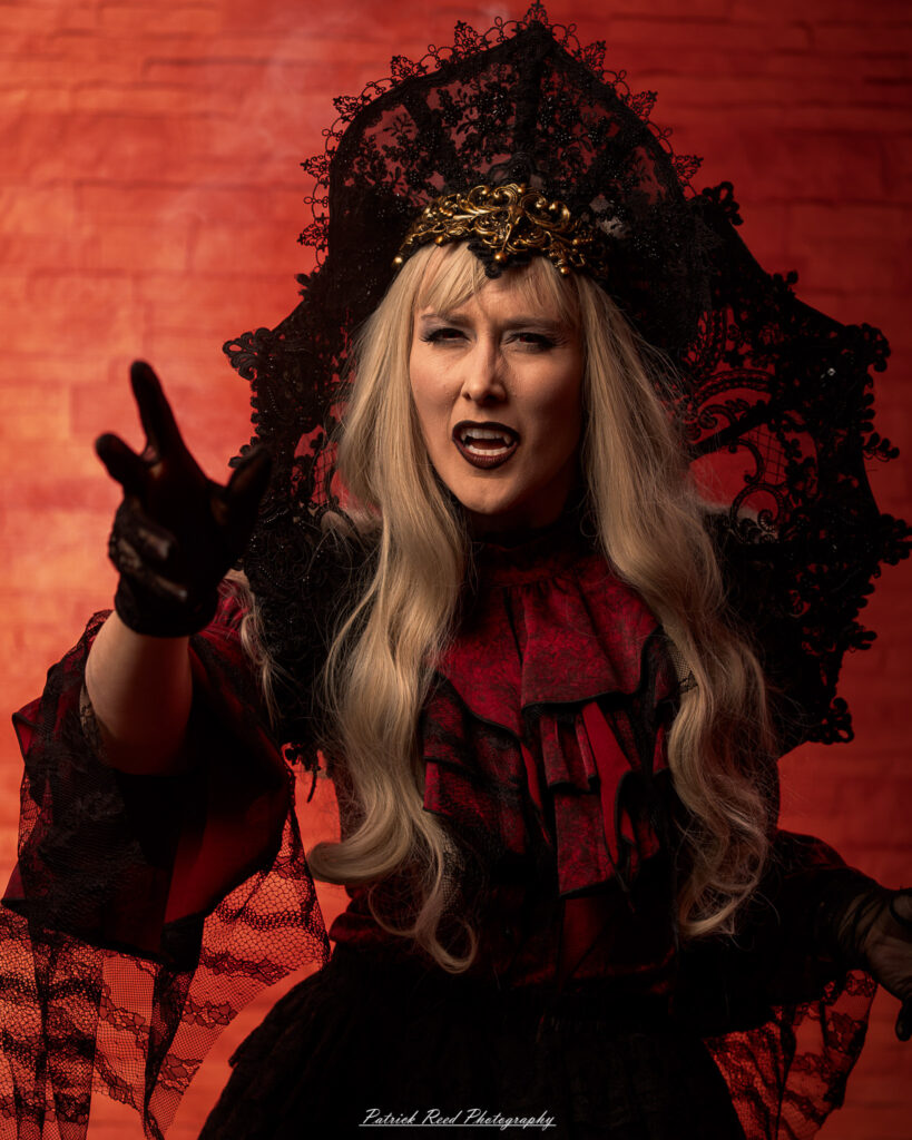 Portrait of a woman in vampire cosplay named Lady Thorn, photographed on June 28, 2025. She is posed against a vivid red background, styled with gothic elements and dramatic expression.