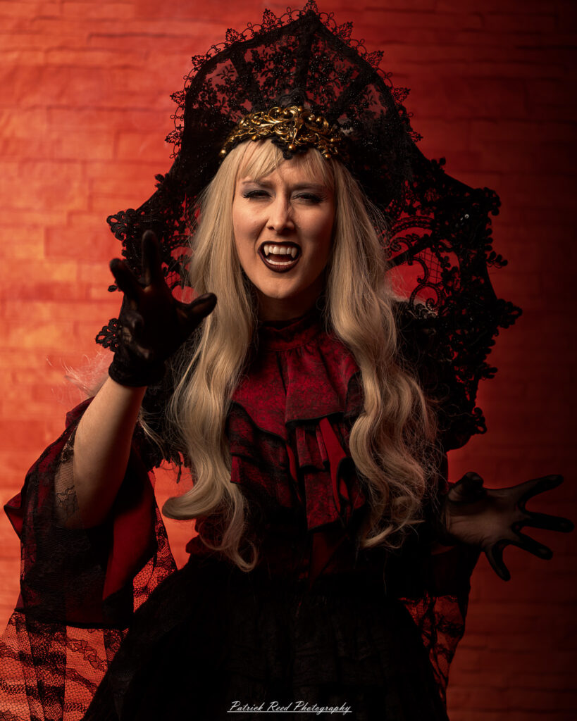 Portrait of a woman in vampire cosplay named Lady Thorn, photographed on June 28, 2025. She is posed against a vivid red background, styled with gothic elements and dramatic expression.