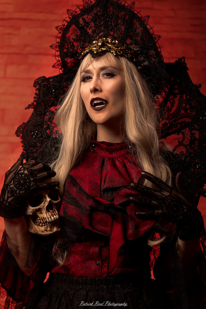 Portrait of a woman in vampire cosplay named Lady Thorn, photographed on June 28, 2025. She is posed against a vivid red background, styled with gothic elements and dramatic expression.