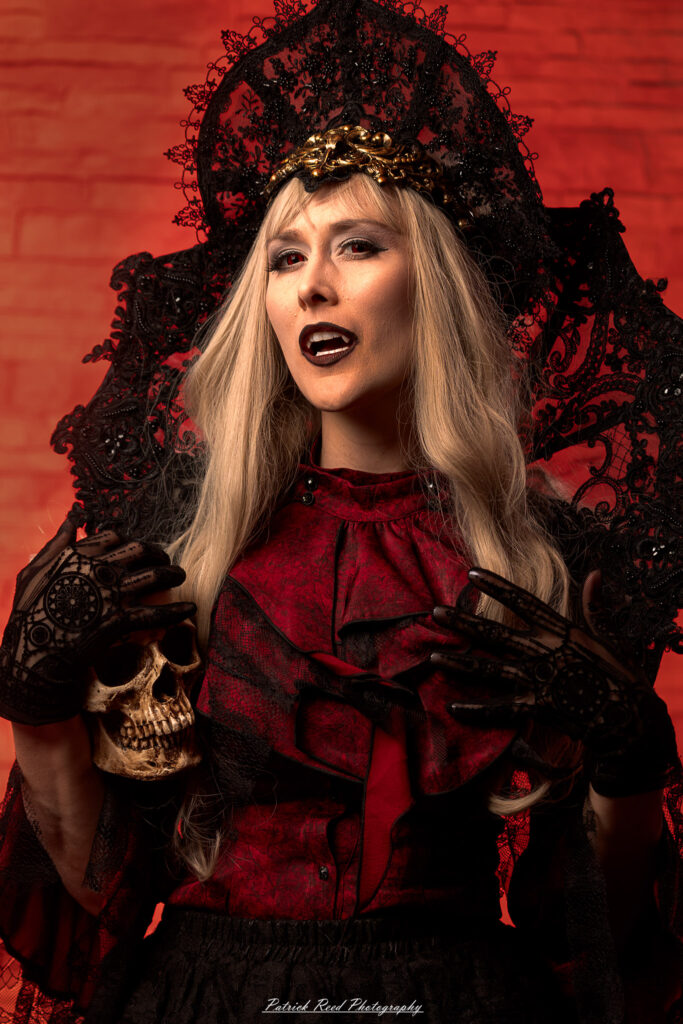 Alt text: Portrait of a woman in vampire cosplay named Lady Thorn, photographed on June 28, 2025. She is posed against a vivid red background, styled with gothic elements and dramatic expression.