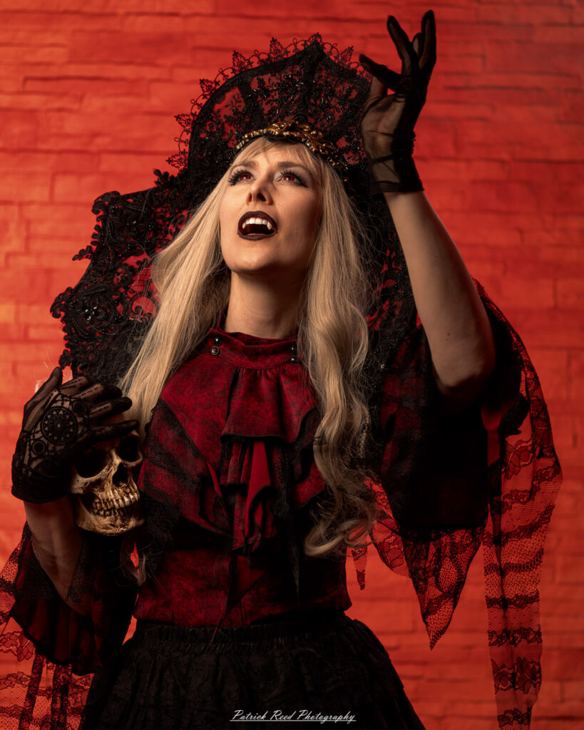 Alt text: Portrait of a woman in vampire cosplay named Lady Thorn, photographed on June 28, 2025. She is posed against a vivid red background, styled with gothic elements and dramatic expression.