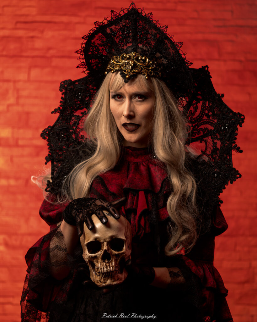 Alt text: Portrait of a woman in vampire cosplay named Lady Thorn, photographed on June 28, 2025. She is posed against a vivid red background, styled with gothic elements and dramatic expression.