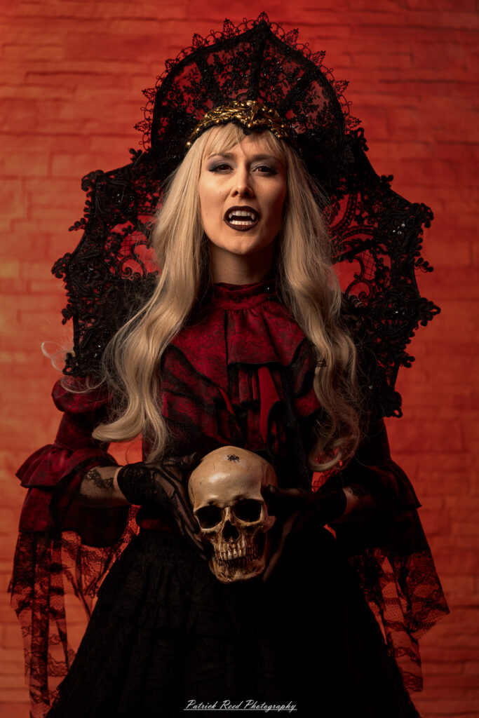 Portrait of a woman in vampire cosplay named Lady Thorn, photographed on June 28, 2025. She is posed against a vivid red background, styled with gothic elements and dramatic expression.