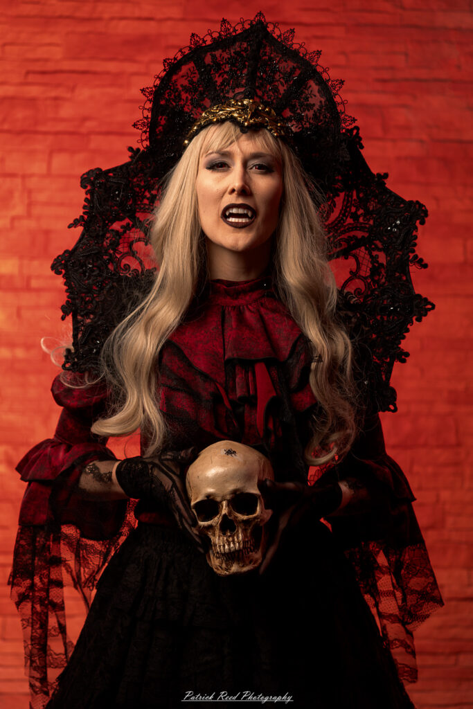 Alt text: Portrait of a woman in vampire cosplay named Lady Thorn, photographed on June 28, 2025. She is posed against a vivid red background, styled with gothic elements and dramatic expression.