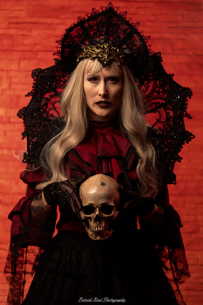 Alt text: Portrait of a woman in vampire cosplay named Lady Thorn, photographed on June 28, 2025. She is posed against a vivid red background, styled with gothic elements and dramatic expression.