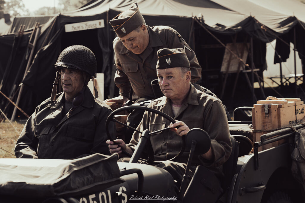 A group of World War II reenactors in period-accurate uniforms—American, German, and French Resistance—on a sandy shore during the D-Day Conneaut 2025 reenactment at Conneaut Township Park, Ohio.