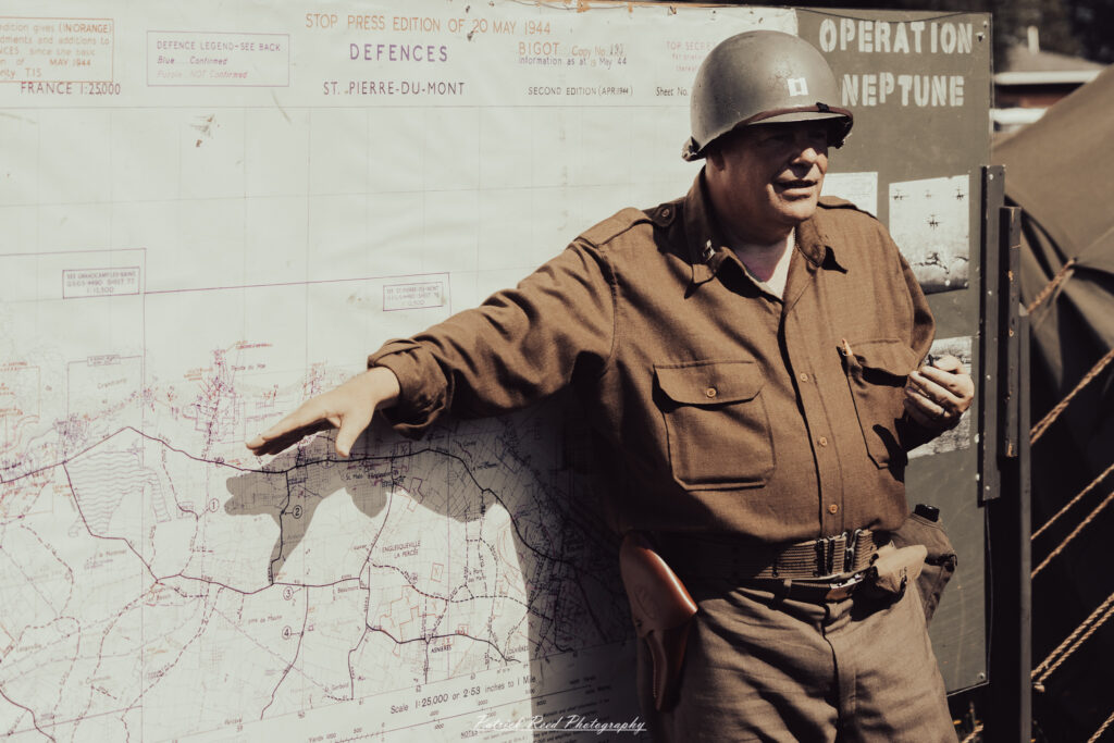 A group of World War II reenactors in period-accurate uniforms—American, German, and French Resistance—on a sandy shore during the D-Day Conneaut 2025 reenactment at Conneaut Township Park, Ohio.