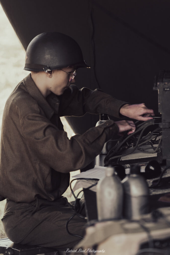 A group of World War II reenactors in period-accurate uniforms—American, German, and French Resistance—on a sandy shore during the D-Day Conneaut 2025 reenactment at Conneaut Township Park, Ohio.