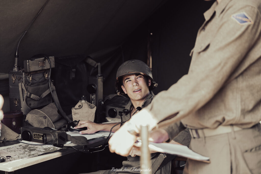A group of World War II reenactors in period-accurate uniforms—American, German, and French Resistance—on a sandy shore during the D-Day Conneaut 2025 reenactment at Conneaut Township Park, Ohio.