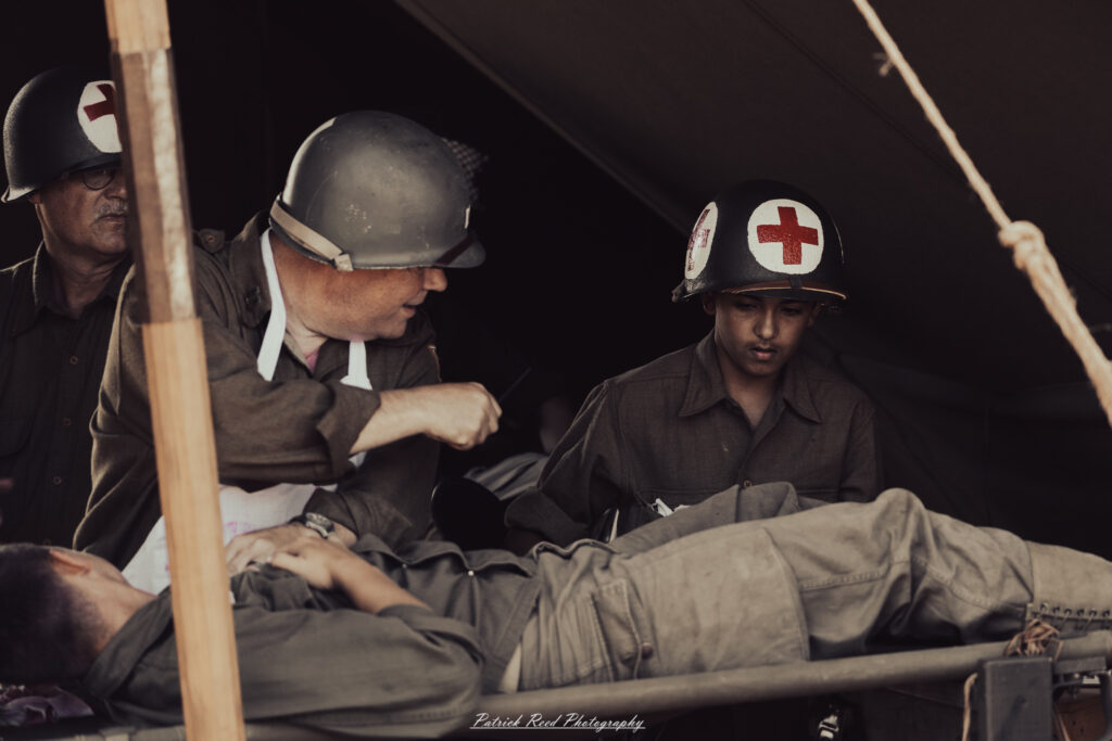 A group of World War II reenactors in period-accurate uniforms—American, German, and French Resistance—on a sandy shore during the D-Day Conneaut 2025 reenactment at Conneaut Township Park, Ohio.