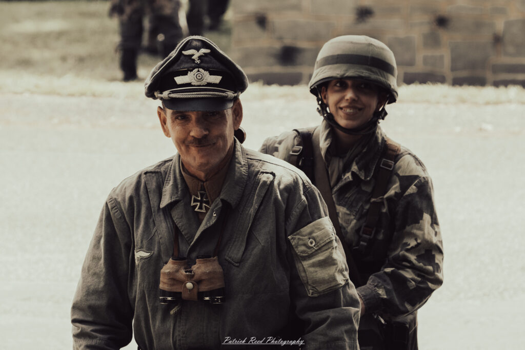 A group of World War II reenactors in period-accurate uniforms—American, German, and French Resistance—on a sandy shore during the D-Day Conneaut 2025 reenactment at Conneaut Township Park, Ohio.