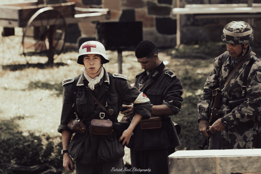 A group of World War II reenactors in period-accurate uniforms—American, German, and French Resistance—on a sandy shore during the D-Day Conneaut 2025 reenactment at Conneaut Township Park, Ohio.