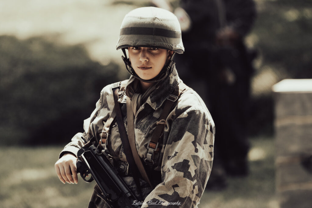 A group of World War II reenactors in period-accurate uniforms—American, German, and French Resistance—on a sandy shore during the D-Day Conneaut 2025 reenactment at Conneaut Township Park, Ohio.