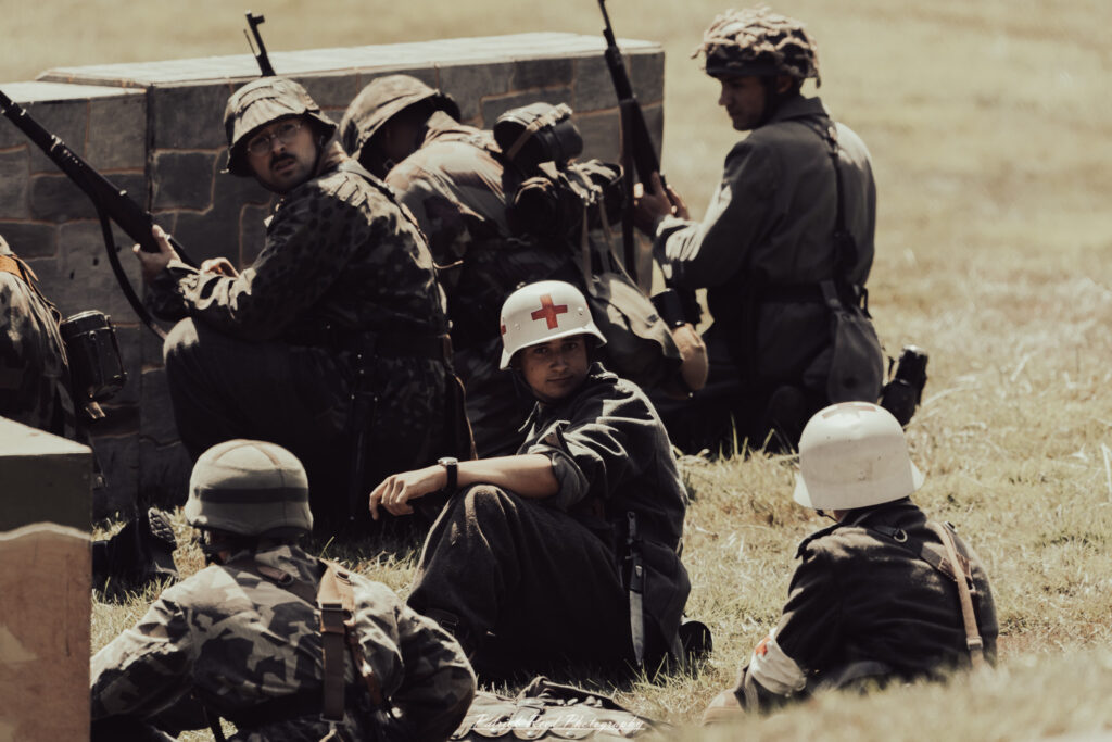 A group of World War II reenactors in period-accurate uniforms—American, German, and French Resistance—on a sandy shore during the D-Day Conneaut 2025 reenactment at Conneaut Township Park, Ohio.