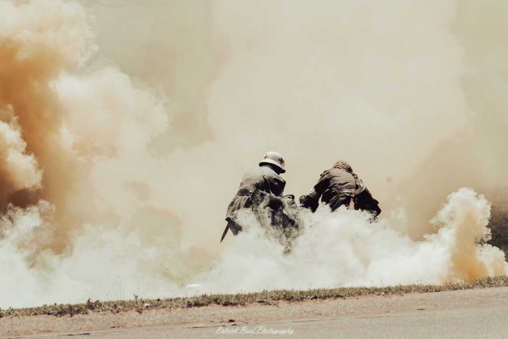 A group of World War II reenactors in period-accurate uniforms—American, German, and French Resistance—on a sandy shore during the D-Day Conneaut 2025 reenactment at Conneaut Township Park, Ohio.