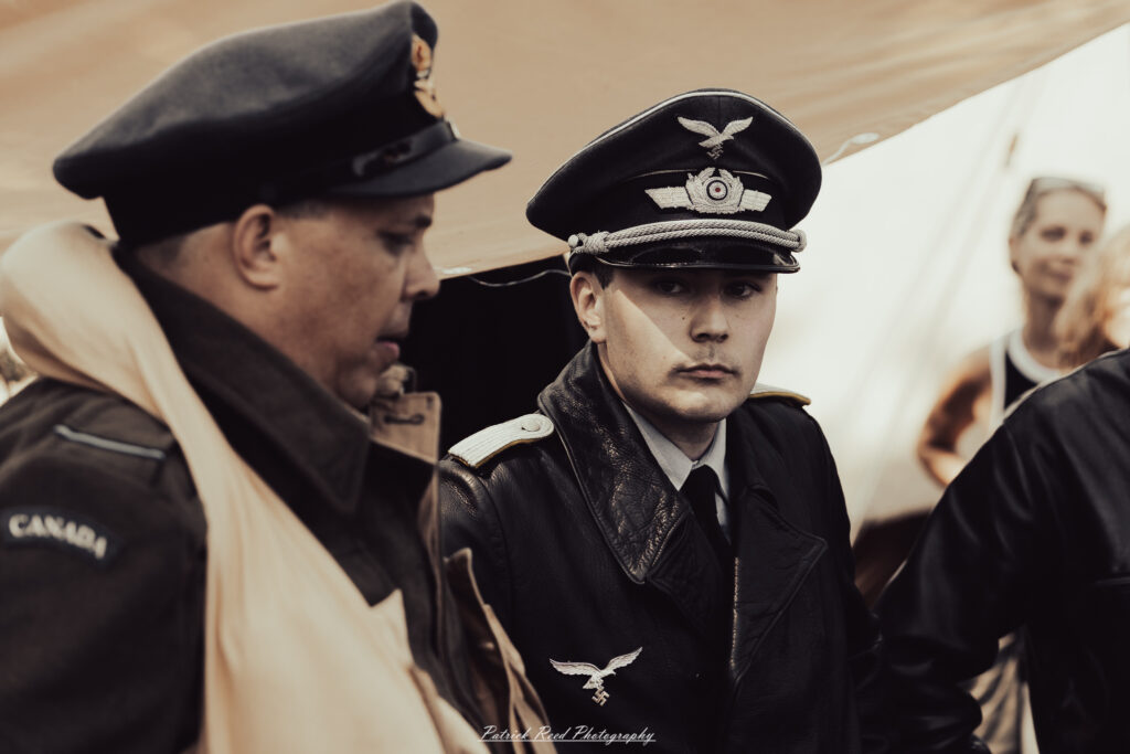 A group of World War II reenactors in period-accurate uniforms—American, German, and French Resistance—on a sandy shore during the D-Day Conneaut 2025 reenactment at Conneaut Township Park, Ohio.