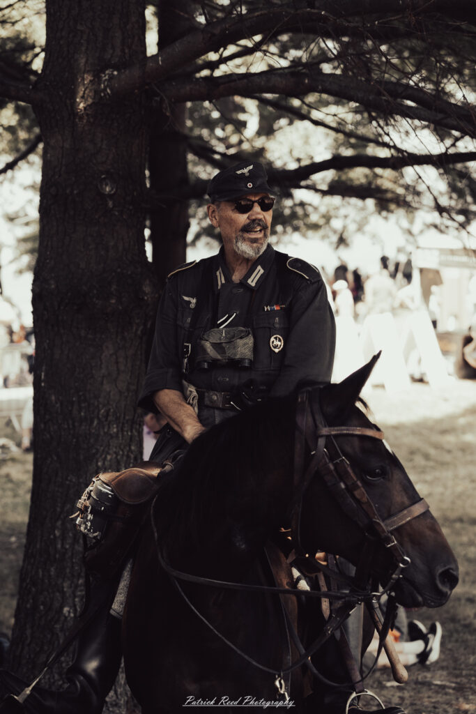 A group of World War II reenactors in period-accurate uniforms—American, German, and French Resistance—on a sandy shore during the D-Day Conneaut 2025 reenactment at Conneaut Township Park, Ohio.