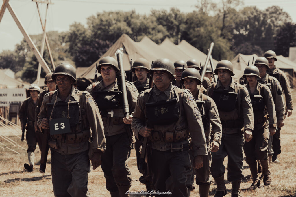 A group of World War II reenactors in period-accurate uniforms—American, German, and French Resistance—on a sandy shore during the D-Day Conneaut 2025 reenactment at Conneaut Township Park, Ohio.
