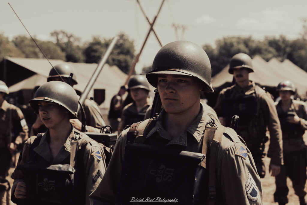 A group of World War II reenactors in period-accurate uniforms—American, German, and French Resistance—on a sandy shore during the D-Day Conneaut 2025 reenactment at Conneaut Township Park, Ohio.
