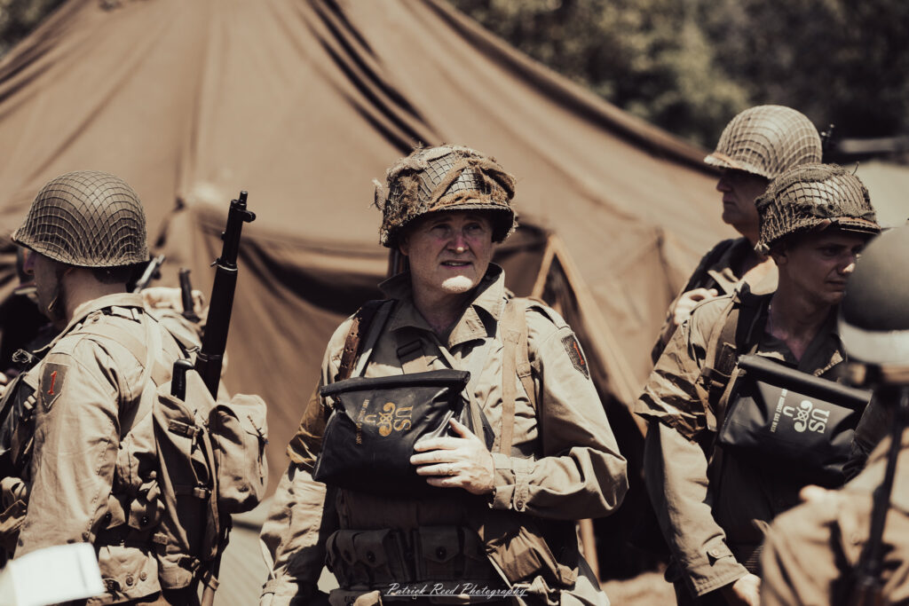 A group of World War II reenactors in period-accurate uniforms—American, German, and French Resistance—on a sandy shore during the D-Day Conneaut 2025 reenactment at Conneaut Township Park, Ohio.