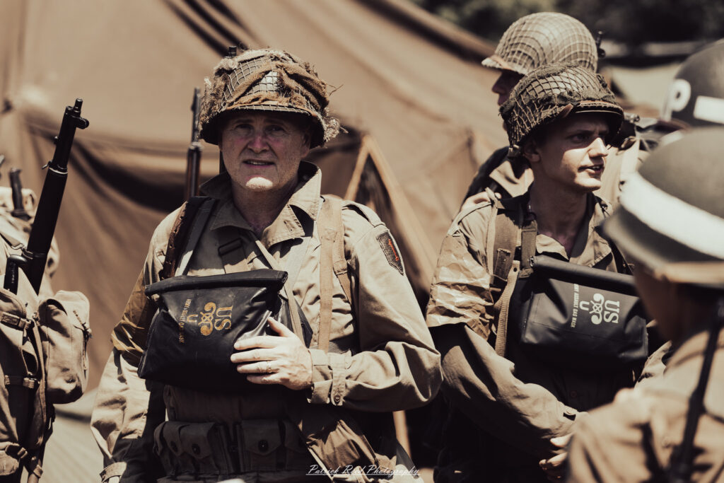 A group of World War II reenactors in period-accurate uniforms—American, German, and French Resistance—on a sandy shore during the D-Day Conneaut 2025 reenactment at Conneaut Township Park, Ohio.