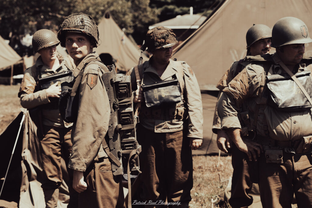 A group of World War II reenactors in period-accurate uniforms—American, German, and French Resistance—on a sandy shore during the D-Day Conneaut 2025 reenactment at Conneaut Township Park, Ohio.