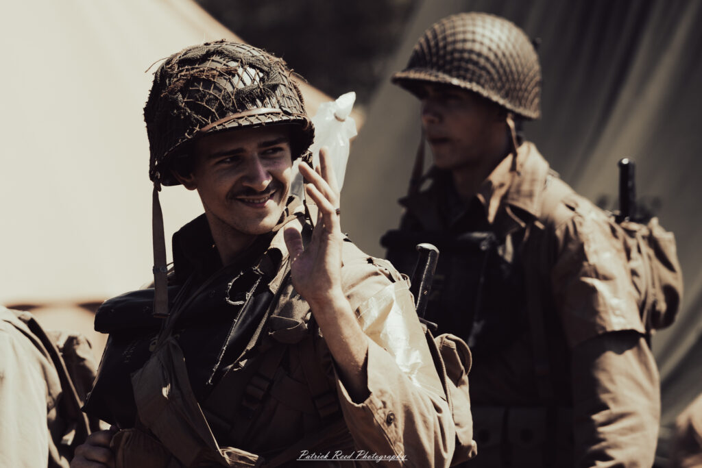 A group of World War II reenactors in period-accurate uniforms—American, German, and French Resistance—on a sandy shore during the D-Day Conneaut 2025 reenactment at Conneaut Township Park, Ohio.