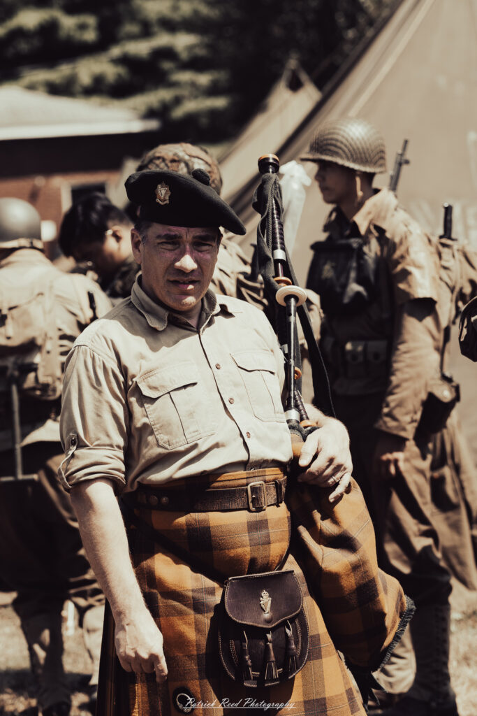 A group of World War II reenactors in period-accurate uniforms—American, German, and French Resistance—on a sandy shore during the D-Day Conneaut 2025 reenactment at Conneaut Township Park, Ohio.