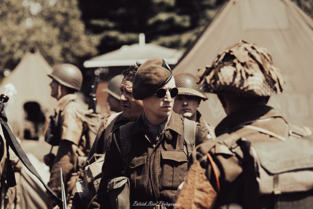 A group of World War II reenactors in period-accurate uniforms—American, German, and French Resistance—on a sandy shore during the D-Day Conneaut 2025 reenactment at Conneaut Township Park, Ohio.