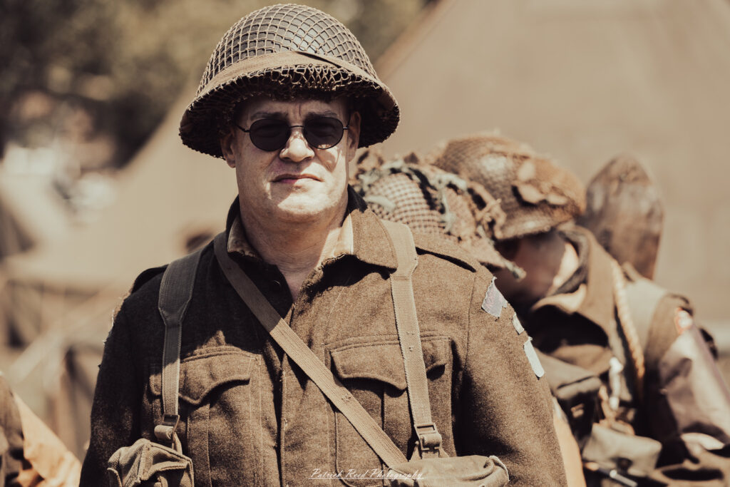 A group of World War II reenactors in period-accurate uniforms—American, German, and French Resistance—on a sandy shore during the D-Day Conneaut 2025 reenactment at Conneaut Township Park, Ohio.