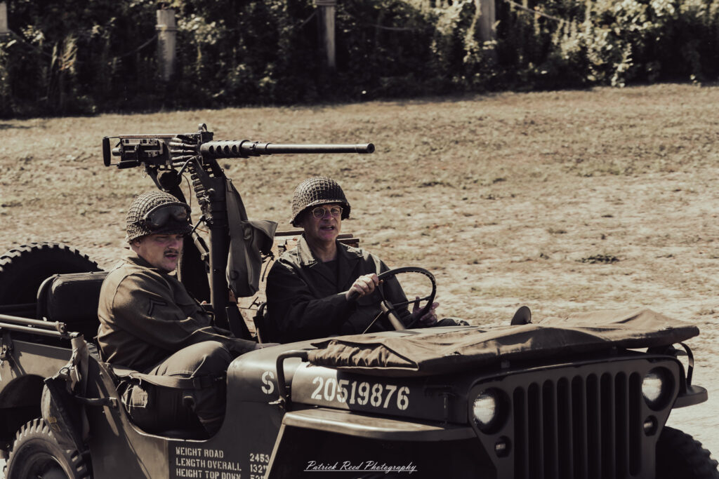 A group of World War II reenactors in period-accurate uniforms—American, German, and French Resistance—on a sandy shore during the D-Day Conneaut 2025 reenactment at Conneaut Township Park, Ohio.