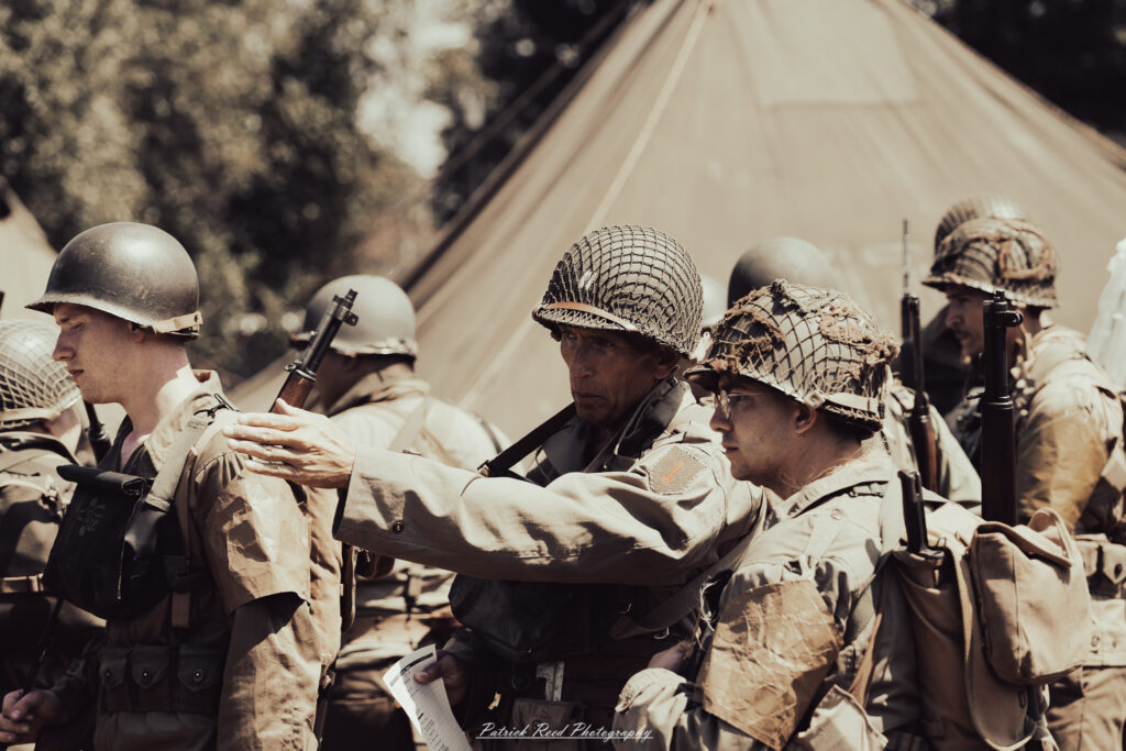 A group of World War II reenactors in period-accurate uniforms—American, German, and French Resistance—on a sandy shore during the D-Day Conneaut 2025 reenactment at Conneaut Township Park, Ohio.