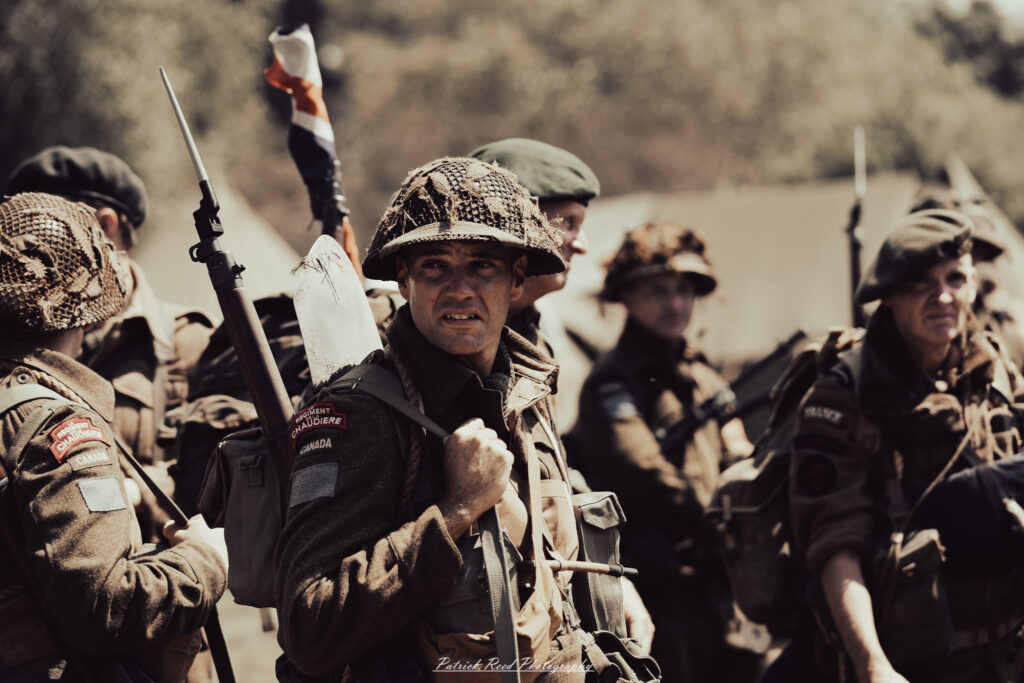 A group of World War II reenactors in period-accurate uniforms—American, German, and French Resistance—on a sandy shore during the D-Day Conneaut 2025 reenactment at Conneaut Township Park, Ohio.