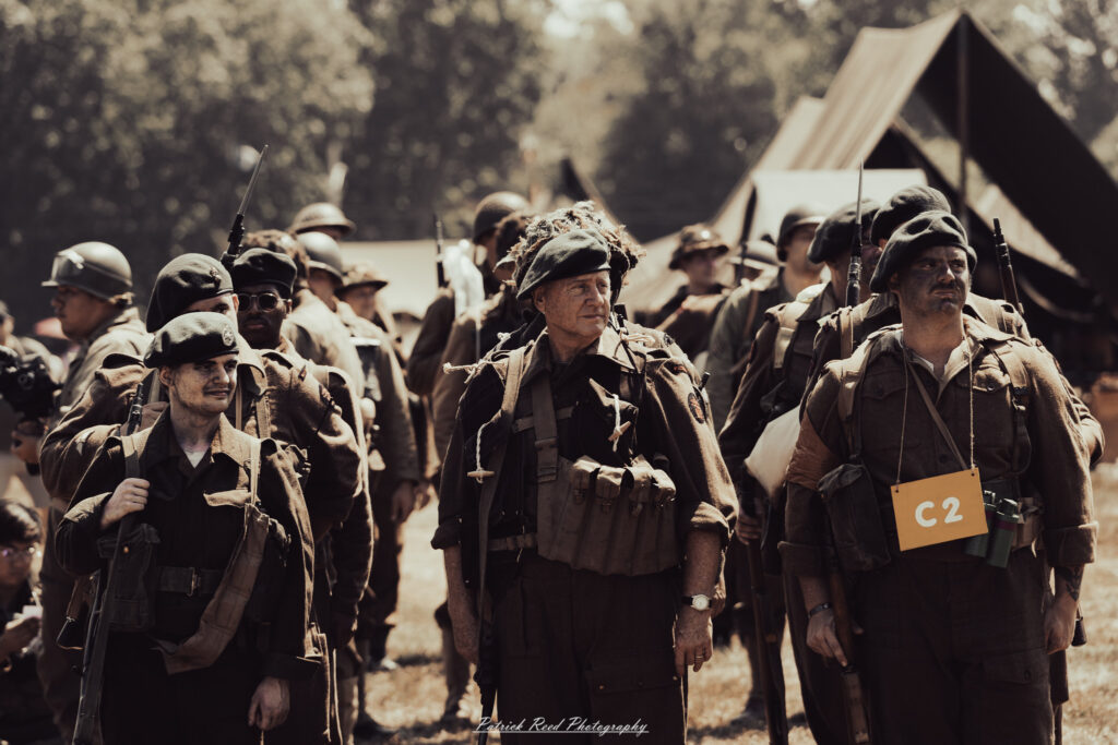 A group of World War II reenactors in period-accurate uniforms—American, German, and French Resistance—on a sandy shore during the D-Day Conneaut 2025 reenactment at Conneaut Township Park, Ohio.