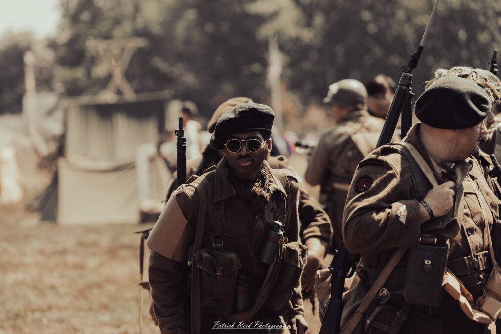 A group of World War II reenactors in period-accurate uniforms—American, German, and French Resistance—on a sandy shore during the D-Day Conneaut 2025 reenactment at Conneaut Township Park, Ohio.