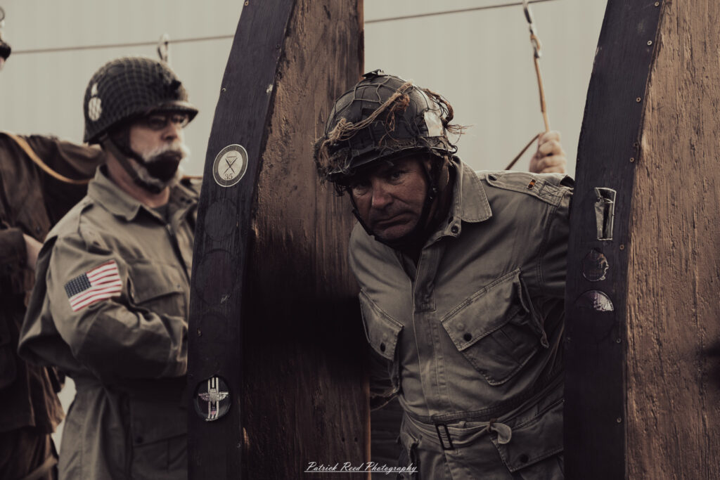A group of World War II reenactors in period-accurate uniforms—American, German, and French Resistance—on a sandy shore during the D-Day Conneaut 2025 reenactment at Conneaut Township Park, Ohio.