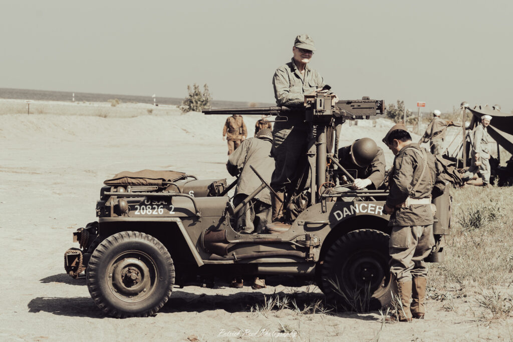 A group of World War II reenactors in period-accurate uniforms—American, German, and French Resistance—on a sandy shore during the D-Day Conneaut 2025 reenactment at Conneaut Township Park, Ohio.