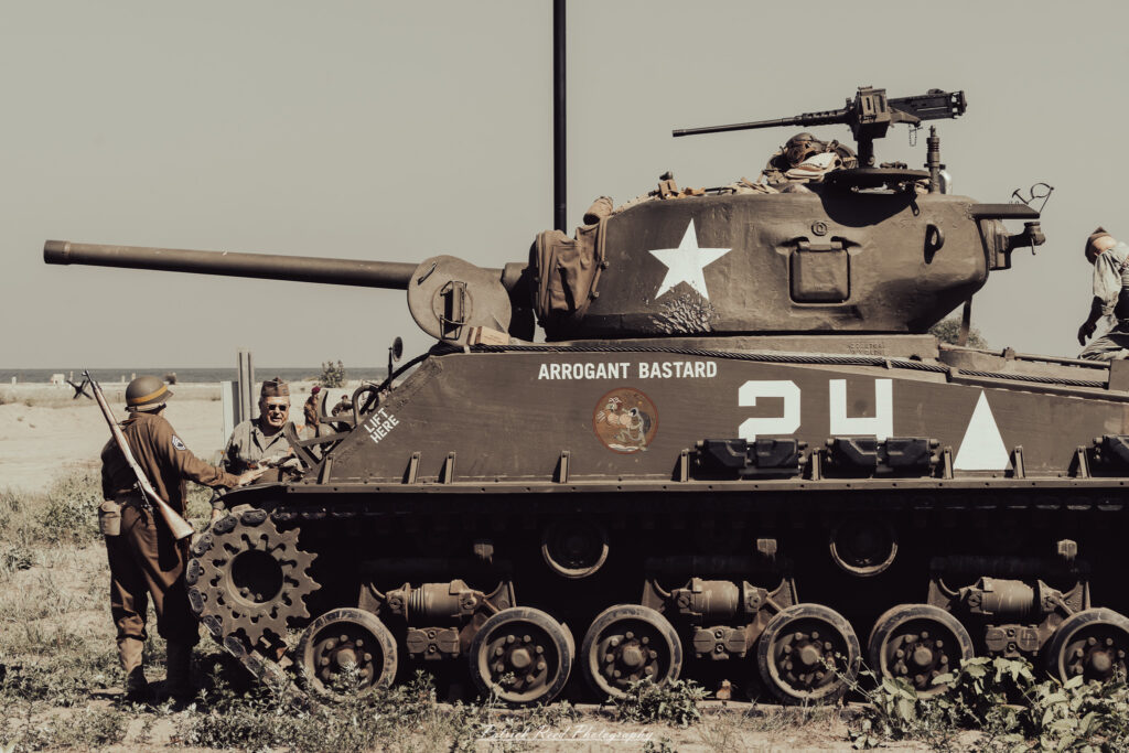 A group of World War II reenactors in period-accurate uniforms—American, German, and French Resistance—on a sandy shore during the D-Day Conneaut 2025 reenactment at Conneaut Township Park, Ohio.
