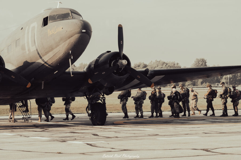 A group of World War II reenactors in period-accurate uniforms—American, German, and French Resistance—on a sandy shore during the D-Day Conneaut 2025 reenactment at Conneaut Township Park, Ohio.
