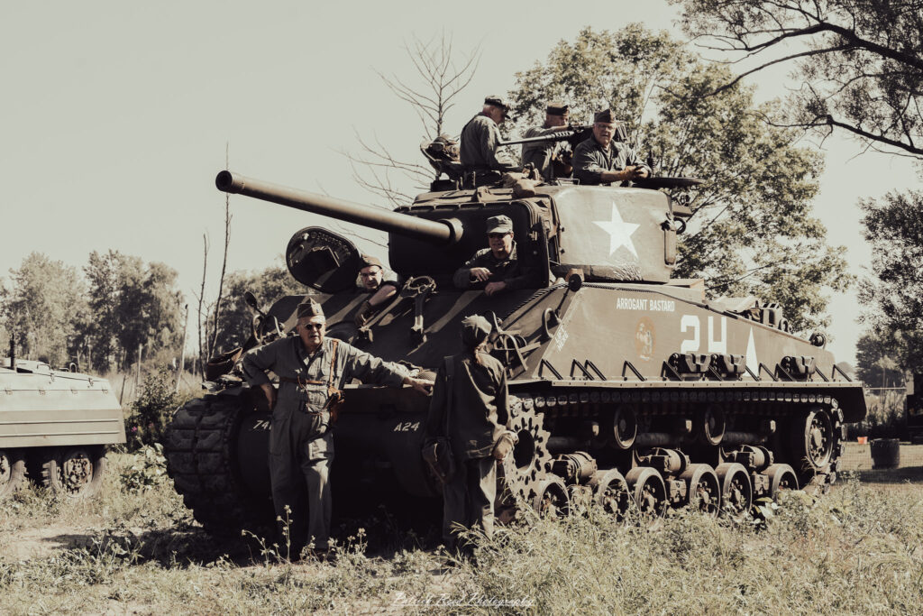 A group of World War II reenactors in period-accurate uniforms—American, German, and French Resistance—on a sandy shore during the D-Day Conneaut 2025 reenactment at Conneaut Township Park, Ohio.