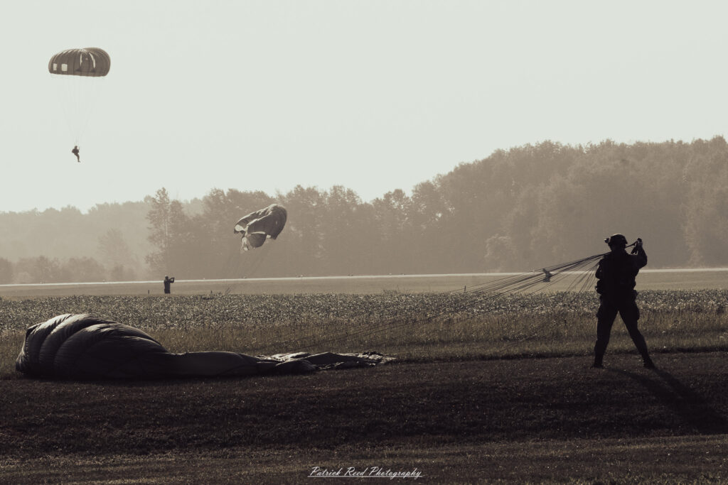 A group of World War II reenactors in period-accurate uniforms—American, German, and French Resistance—on a sandy shore during the D-Day Conneaut 2025 reenactment at Conneaut Township Park, Ohio.
