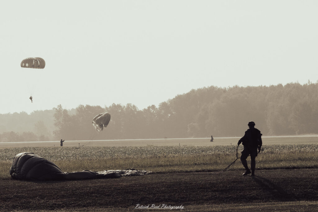 A group of World War II reenactors in period-accurate uniforms—American, German, and French Resistance—on a sandy shore during the D-Day Conneaut 2025 reenactment at Conneaut Township Park, Ohio.