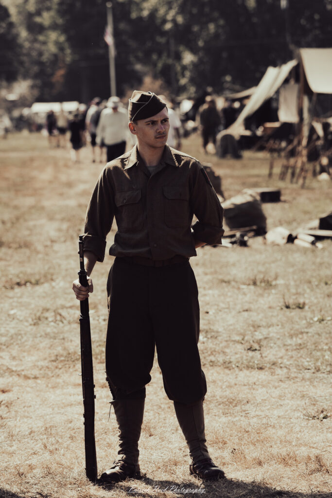 A group of World War II reenactors in period-accurate uniforms—American, German, and French Resistance—on a sandy shore during the D-Day Conneaut 2025 reenactment at Conneaut Township Park, Ohio.