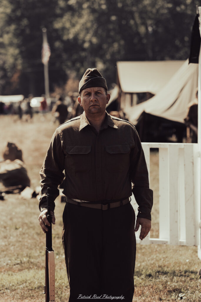 A group of World War II reenactors in period-accurate uniforms—American, German, and French Resistance—on a sandy shore during the D-Day Conneaut 2025 reenactment at Conneaut Township Park, Ohio.