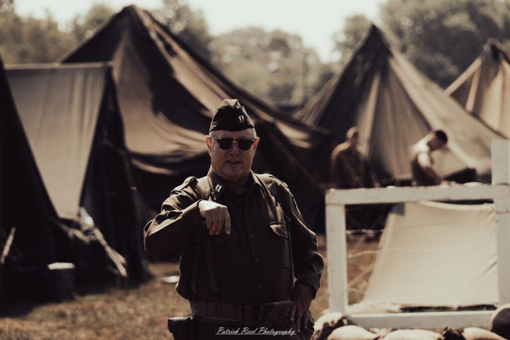 A group of World War II reenactors in period-accurate uniforms—American, German, and French Resistance—on a sandy shore during the D-Day Conneaut 2025 reenactment at Conneaut Township Park, Ohio.