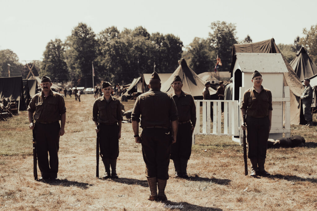 A group of World War II reenactors in period-accurate uniforms—American, German, and French Resistance—on a sandy shore during the D-Day Conneaut 2025 reenactment at Conneaut Township Park, Ohio.