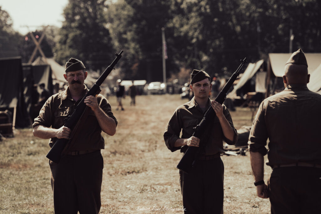 A group of World War II reenactors in period-accurate uniforms—American, German, and French Resistance—on a sandy shore during the D-Day Conneaut 2025 reenactment at Conneaut Township Park, Ohio.