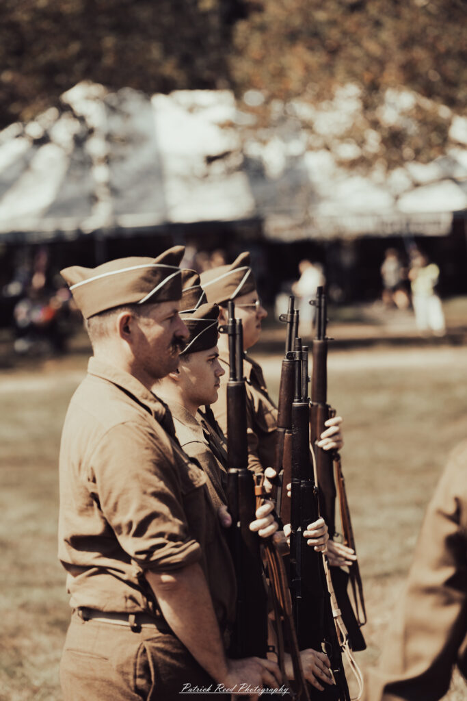 A group of World War II reenactors in period-accurate uniforms—American, German, and French Resistance—on a sandy shore during the D-Day Conneaut 2025 reenactment at Conneaut Township Park, Ohio.